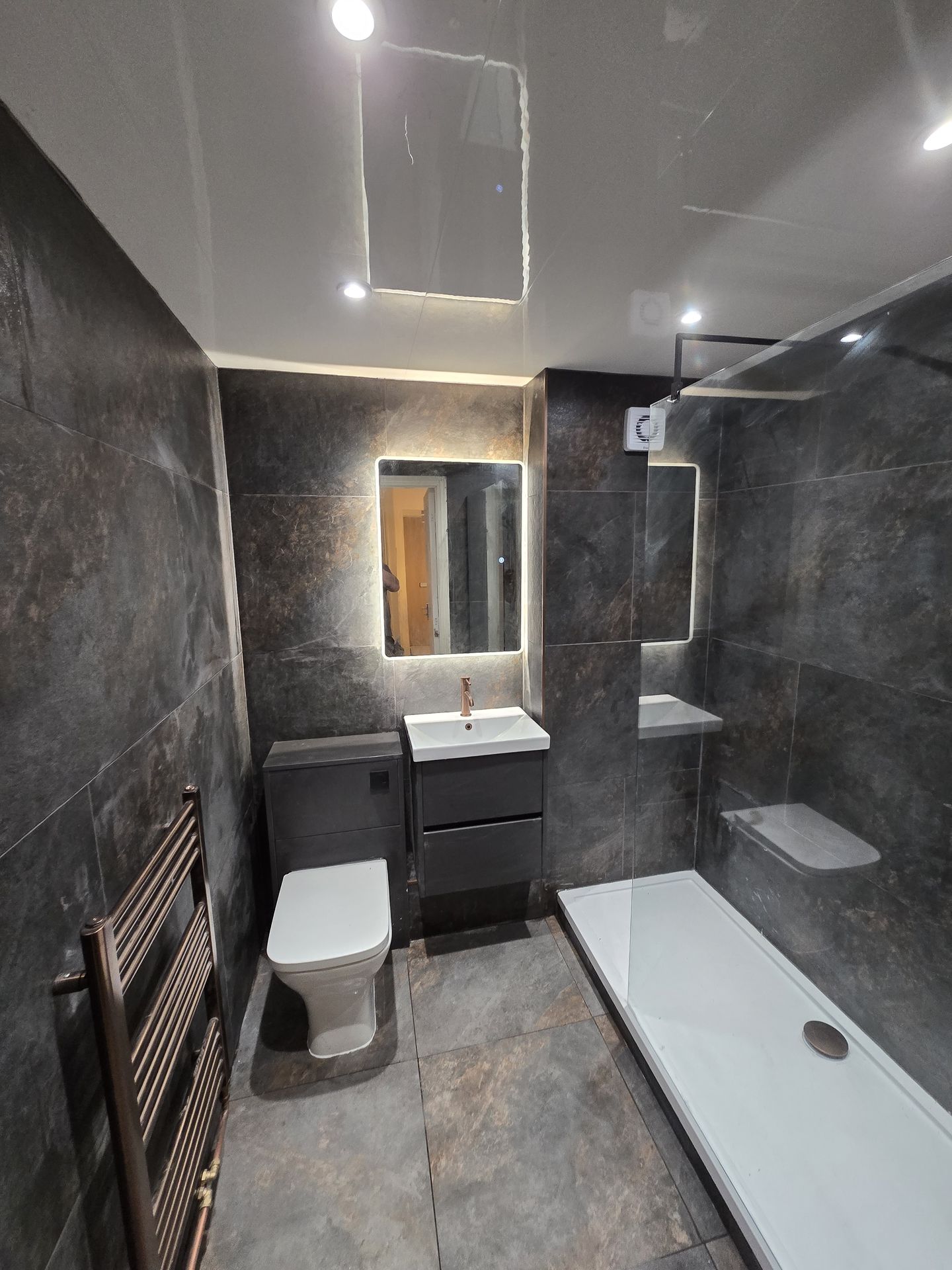 Slate tiled bathroom with backlit mirror and vanity unit